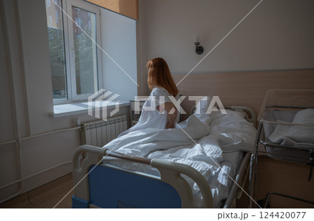 An unhappy woman sits on a couch and holds her stomach in a hospital room after giving birth. An unhappy woman sits on a couch and holds her stomach in a hospital room after giving birth. 124420077