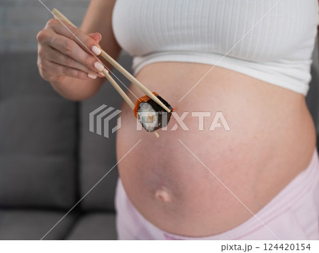 A pregnant woman holds a roll with chopsticks. Close-up of the belly. A pregnant woman holds a roll with chopsticks. Close-up of the belly. 124420154