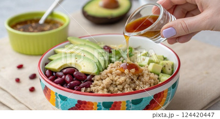 A closeup of a s lifting apple cider vinegar from a small dish ready to mix into a colorful grain bowl filled with quinoa avocado and beans.. A closeup of a s lifting apple cider vinegar from a small dish ready to mix into a colorful grain bowl filled with quinoa avocado and beans.. 124420447