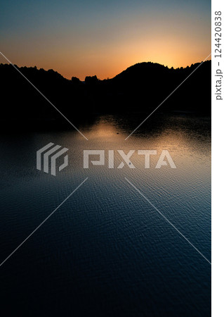 湖面を吹き渡る風 　2025年春奈良布目ダムにて　山際に沈む夕日と黄金色に染まる空と湖面③ 124420838