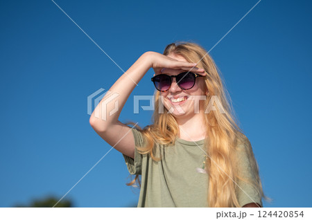 Smiling young woman with sunglasses under clear blue sky. 124420854