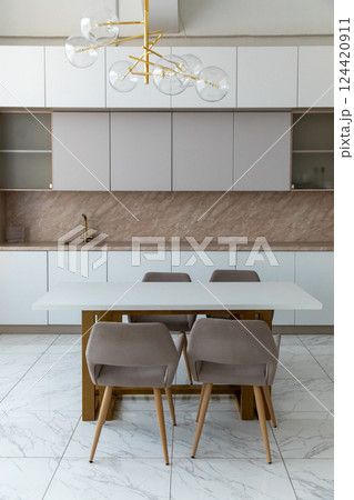 A modern, spacious kitchen with light facades, wooden trim, marble tiles, a table, upholstered chairs, an empty countertop. Minimalistic design. A modern, spacious kitchen with light facades, wooden trim, marble tiles, a table, upholstered chairs, an empty countertop. Minimalistic design. 124420911