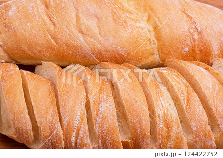 Wheat baguette sliced and whole close-up as a background. Wheat baguette sliced and whole close-up as a background. 124422752