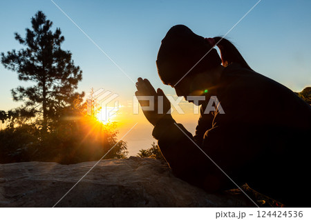 Silhouette of christian woman prayer on sunset background. Woman raising his hands in worship for peaceful life. Female praising God on the mountain. Christian religion concept. 124424536