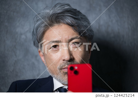 スマホを持つカメラ目線のグレイヘアの社長や経営者のシニア男性イメージのクローズアップ スマホを持つカメラ目線のグレイヘアの社長や経営者のシニア男性イメージのクローズアップ 124425214