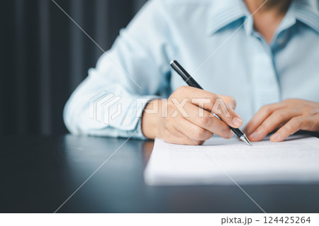 Close up businesswoman signing documents. Hand of woman write business document charts at office desk. Woman signing document, focus on female hand holding pen, putting signature at official paper. 124425264
