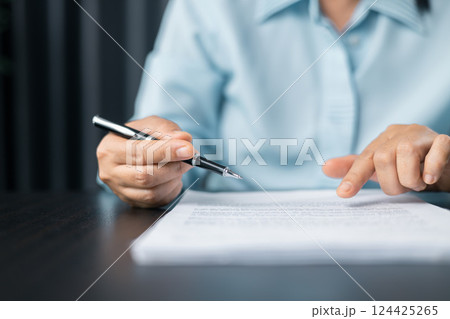 Woman signing document, focus on female hand holding pen, putting signature at official paper. Close up businesswoman signing documents. Hand of woman write business document charts at office desk. 124425265