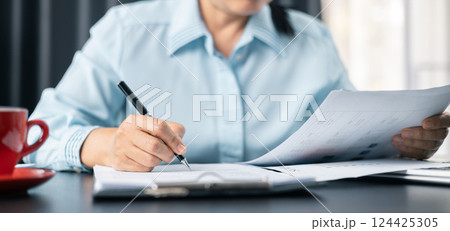 Woman signing document, focus on female hand holding pen, putting signature at official paper. Close up businesswoman signing documents. Hand of woman write business document charts at office desk. 124425305