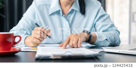 Woman signing document, focus on female hand holding pen, putting signature at official paper. Close up businesswoman signing documents. Hand of woman write business document charts at office desk. 124425418
