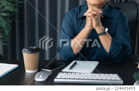 Woman with hands clasped praying while sitting at desk in office. Businesswoman praying at work. Contemplative prayer thinking in office. Hands folded in prayer gesture beg about something. 124425455