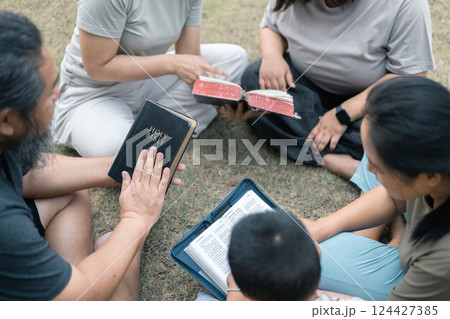 Young woman held her mother's hand in prayer, surrounded by their outdoor community, where love and family life flourished through shared moments of prayer and support. Group christian pray concept. 124427385