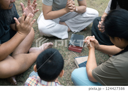 Young woman held her mother's hand in prayer, surrounded by their outdoor community, where love and family life flourished through shared moments of prayer and support. Group christian pray concept. 124427386