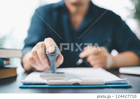 Businesswoman confidently placed her stamp of approval on legal document, finalizing the contract and solidifying the agreement in office with her authority. document, approve, business, stamp. 124427710