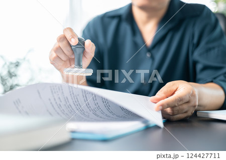 Businesswoman confidently placed her stamp of approval on legal document, finalizing the contract and solidifying the agreement in office with her authority. document, approve, business, stamp. 124427711
