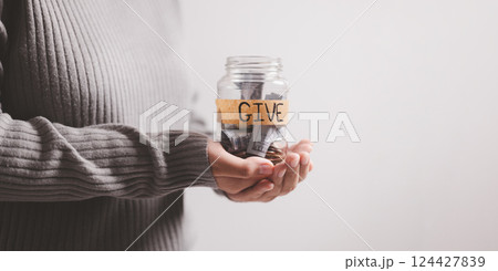 Woman held jar filled with cash with words in bold lettering urging people to donate money, extending her hand in gesture of giving part of her business's charitable efforts. banner with copy space. Woman held jar filled with cash with words in bold lettering urging people to donate money, extending her hand in gesture of giving part of her business's charitable efforts. banner with copy space. 124427839