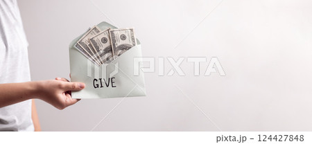 Woman's hand holding dollar bills in envelope with the letters word give, extended her hand to donate cash, promoting the spirit of giving in her business. banner with copy space. Woman's hand holding dollar bills in envelope with the letters word give, extended her hand to donate cash, promoting the spirit of giving in her business. banner with copy space. 124427848