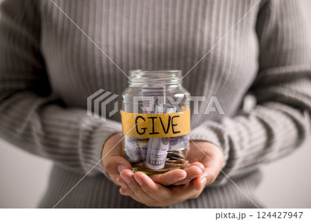 Woman holding coins and cash in jar with words Give or Donate elegantly lettered on its front, embodying spirit of giving. words, lettering, donate, jar, money, giving, woman, give, coin. 124427947