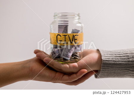 Woman holding coins and cash in jar with words Give or Donate elegantly lettered on its front, embodying spirit of giving. words, lettering, donate, jar, money, giving, woman, give, coin. Woman holding coins and cash in jar with words Give or Donate elegantly lettered on its front, embodying spirit of giving. words, lettering, donate, jar, money, giving, woman, give, coin. 124427953