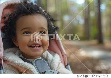 Happy kid in a stroller. The cheerful child in a stroller smiles brightly, showcasing pure happiness during their outdoor outing. Happy kid in a stroller. The cheerful child in a stroller smiles brightly, showcasing pure happiness during their outdoor outing. 124429393