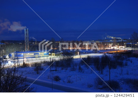A serene winter night scene with vibrant industrial activity in a tranquil snowy landscape 124429451