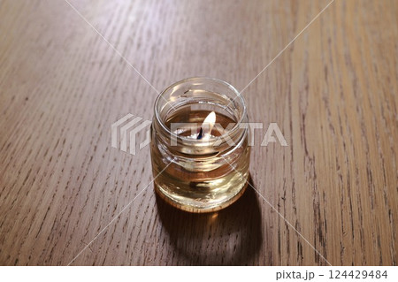 A soothing candle elegantly placed in a glass jar resting on a beautiful wooden surface A soothing candle elegantly placed in a glass jar resting on a beautiful wooden surface 124429484