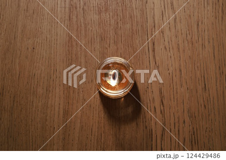 A Beautifully Illuminating Candle with a Warm Glow on a Rustic Wooden Table Surface 124429486