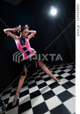 beautiful brunette in pink and black dress and silver shoes on dark background in haze in studio. sensual latino dance, photo in motion 124429993