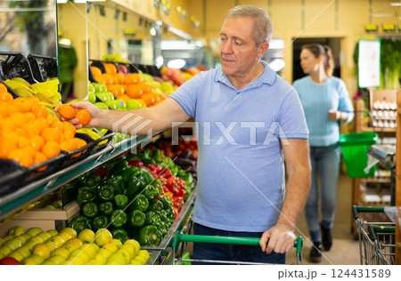Elderly male pensioner in casual wear choosing tangerines in supermarket Elderly male pensioner in casual wear choosing tangerines in supermarket 124431589