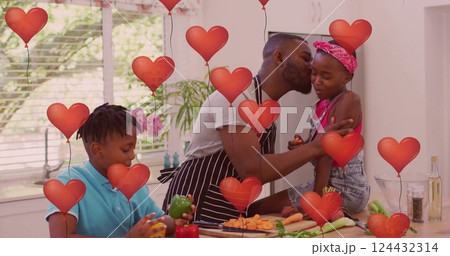 Father kissing daughter in kitchen, hearts image over family cooking together 124432314