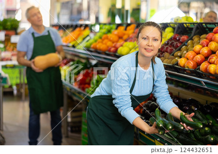 Portrait of smiling busy female merchandiser with cucumber in hands at grocery supermarket Portrait of smiling busy female merchandiser with cucumber in hands at grocery supermarket 124432651