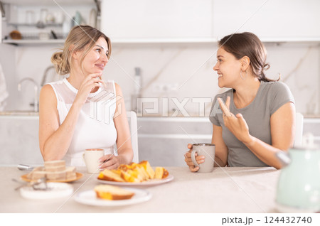 Girlfriends laugh and talk at table with tea and treats 124432740
