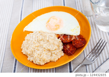 Homemade hearty breakfast - boiled oatmeal, fried eggs with chorizo sausage. Spanish dish Homemade hearty breakfast - boiled oatmeal, fried eggs with chorizo sausage. Spanish dish 124432835