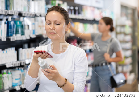 Woman customer using phone to search information about selected product at pharmacy Woman customer using phone to search information about selected product at pharmacy 124432873