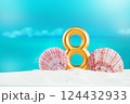 Golden number eight stands on soft white sand, by large pink seashells, against backdrop of calm blue sea on sunny day. Celebration, nature beaut 124432933