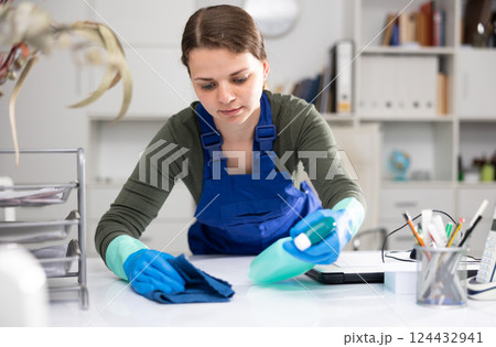 Woman in an overalls cleans the table at office Woman in an overalls cleans the table at office 124432941