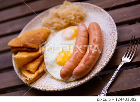 Fried sausages with scrambled eggs, pancakes and cabbage on a wooden background Fried sausages with scrambled eggs, pancakes and cabbage on a wooden background 124433082