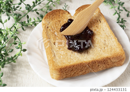 瓶詰めのブルーベリージャムをトーストした食パンに塗る 124433131