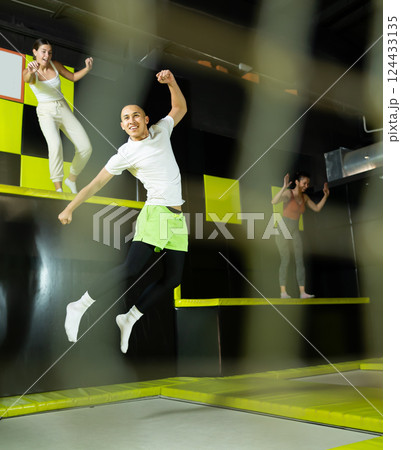 Cheerful young man jumping in modern indoor trampoline park Cheerful young man jumping in modern indoor trampoline park 124433135