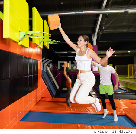Cheerful girl throwing foam cube into basketball hoop in trampoline park 124433170