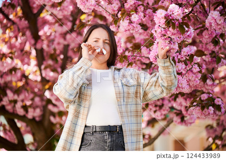 Woman allergic suffering from seasonal allergy and runny nose disease at spring. Young woman with paper tissues inserted into nose - symbolic gesture of inability to breathe due to nasal congestion. Woman allergic suffering from seasonal allergy and runny nose disease at spring. Young woman with paper tissues inserted into nose - symbolic gesture of inability to breathe due to nasal congestion. 124433989