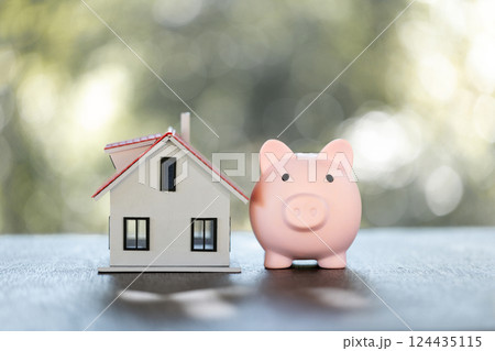 Model of house with piggy bank on table on blurred background. Money saving or investing for home loan or real estate. Investment property, Saving money for retirement concept. 124435115
