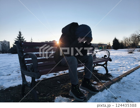 Profile of a sad man complaining sitting on a bench alone in a winter town. lonely guy in the winter park is depressed. Teenage boy alone in the park in the evening. Profile of a sad man complaining sitting on a bench alone in a winter town. lonely guy in the winter park is depressed. Teenage boy alone in the park in the evening. 124435388