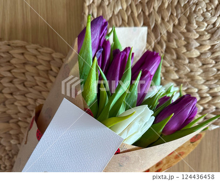 Purple and white tulip bouquet with greeting card on woven background. Seasonal floral gift and heartfelt personal message. Purple and white tulip bouquet with greeting card on woven background. Seasonal floral gift and heartfelt personal message. 124436458