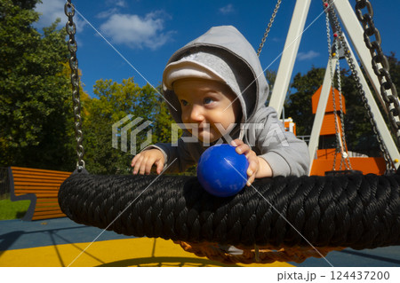 Little girl in sunglasses sits on a rope swing at the playground 124437200