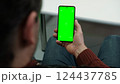 Hand of young man holding smartphone green screen in business office work. Mobile phone vertical mockup. Male person using phone with blank green background display. Chroma key smart phone. Close up. 124437785