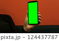 Young woman at work in office holding green mockup smartphone in hand. Woman using mobile phone with chroma key. Vertical mode. Touching, swiping display, pressing, surfing social media. Close-up 124437787