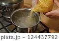 A woman carefully pours golden granules of pasta, couscous, Israeli ptitim or fregola from a transparent bag into a pot of boiling water. Food advertising, restaurant business. Healthy eating 124437792
