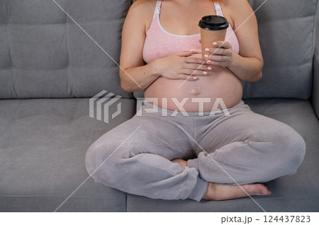Faceless pregnant woman in 3rd trimester holding a coffee glass on her belly. Faceless pregnant woman in 3rd trimester holding a coffee glass on her belly. 124437823