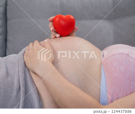 Caucasian pregnant woman holding heart on belly background. Third trimester.  124437886