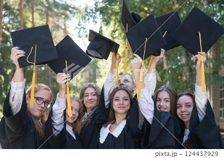 Classmates in graduation gowns throwing hats outdoors.  124437929